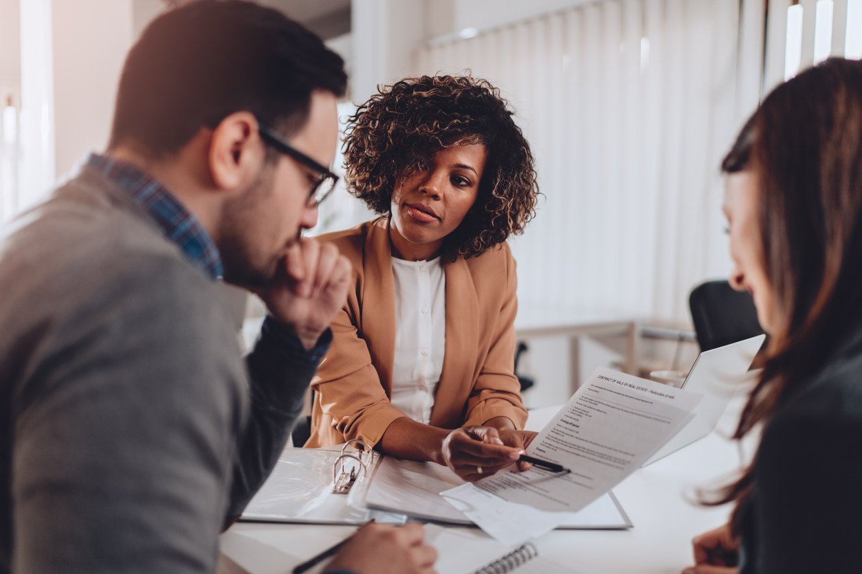 couple going through home buying process | african american mortgage lending office holds document for couple to review.